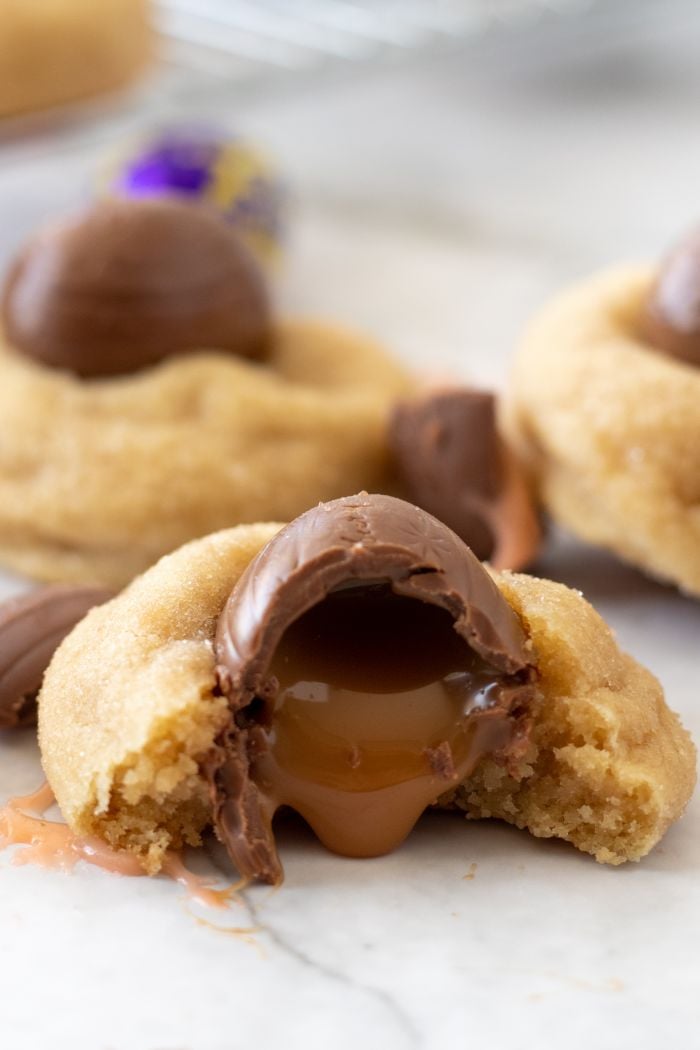 Caramilk egg topped cookie has a bite taken out of it and the caramel is dripping onto the table